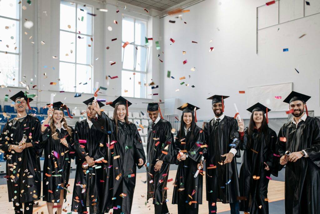 Joyful graduates celebrate commencement with confetti indoors, symbolizing achievement and diversity.